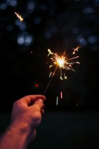 A person holding a bright sparkler outdoors in a festive night setting.