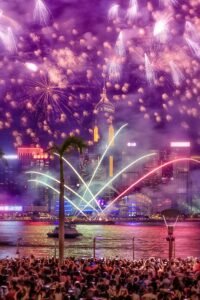 Vibrant fireworks light up the night sky over a bustling city waterfront, capturing a moment of festive celebration.