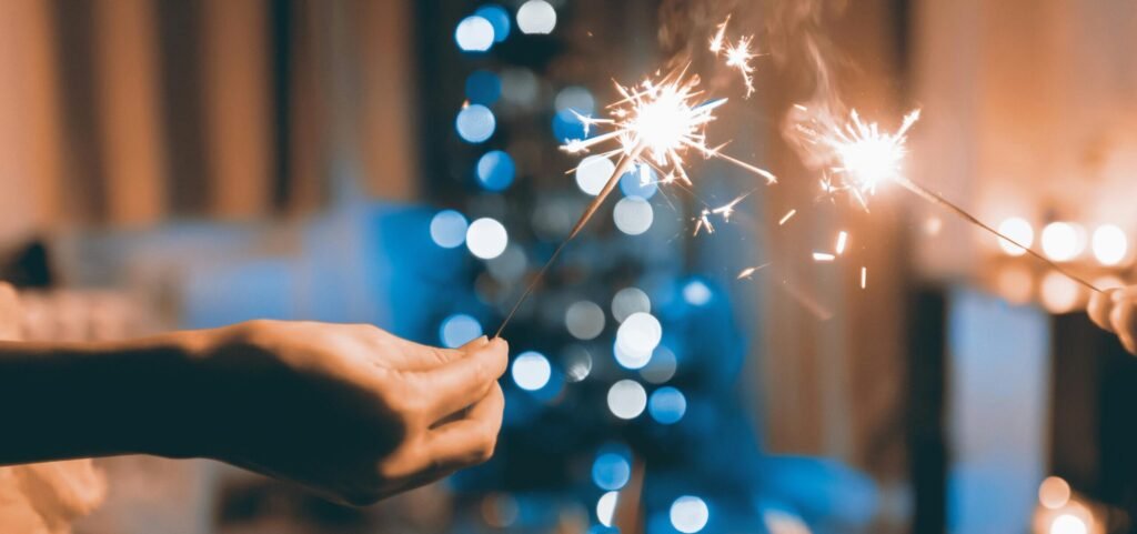 Hands holding sparklers in a festive indoor setting with blurred lights and bokeh effect.